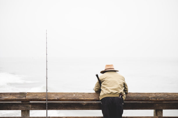 一个渔民靠在码头的木栏杆上看海岸的后景图片下载
