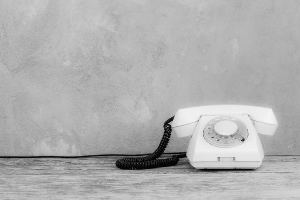 老式白色旋转拨号电话在木制桌子前面灰色混凝土背景。黑白照片。图片下载