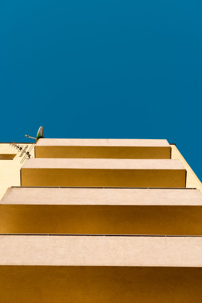 从蓝色的天空下看，现代主义的廉租房被漆成黄色。阳台的砖栏杆。卫星天线挂在墙上。波兰卡托维兹、西里西亚。图片下载