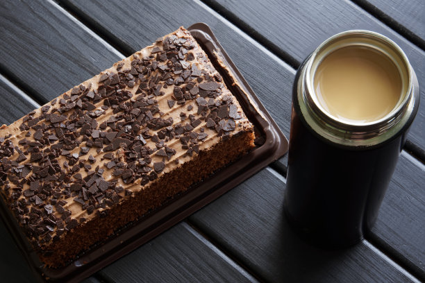 黑木桌上放着一只装着咖啡和牛奶的旅行小保温瓶，旁边放着一块巧克力饼干。在旅游期间或在生态办公室吃饭的概念。图片下载