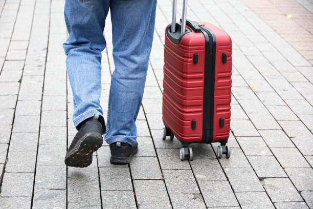 穿着牛仔裤的男人带着带轮子的红色行李箱走着图片下载