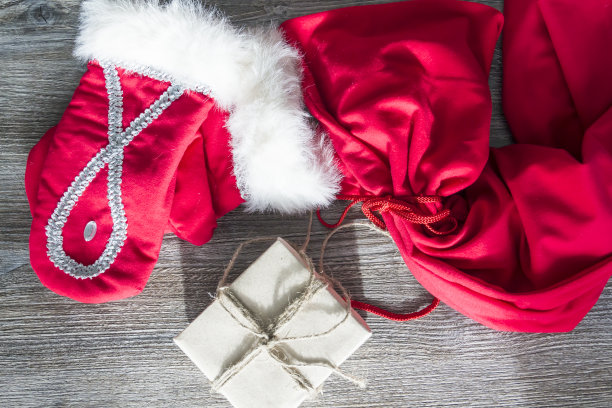 红色的圣诞老人手套和一个木制表面的工艺包装的礼物盒子。图片下载