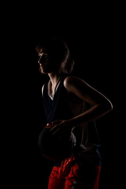 女篮球运动员。美丽的女孩拿着球。侧面照明半剪影工作室肖像对黑色背景。图片下载