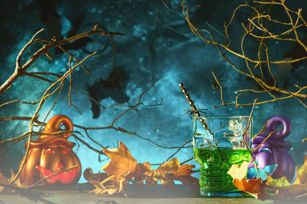 万圣节血腥的鸡尾酒。万圣节绿色鸡尾酒玻璃高脚杯和瓶子形状的头骨在黑暗的背景。有糖果眼睛，蝙蝠，蜘蛛的万圣节派对。亡灵节。Clous-up。图片下载