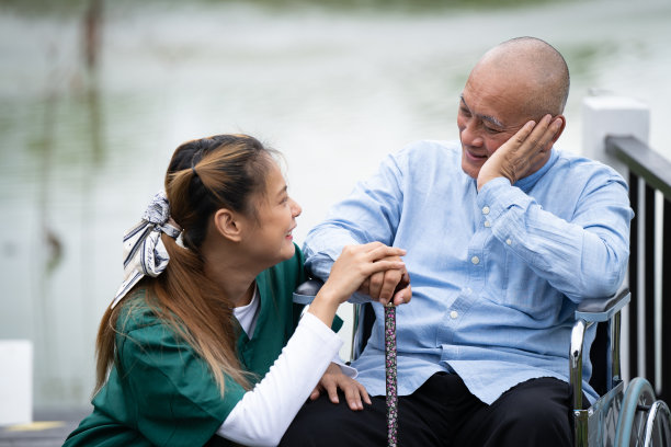 美丽的护士和坐在轮椅上的老人在公园游泳池边的桥上开心地笑着。图片下载