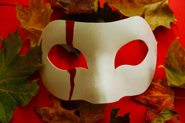 神秘的幽灵白色面具滴血和棕色和黄色的秋叶在红色的背景恐怖万圣节。秋叶，白杨叶为阴森节日为秋季电影-恐怖和惊悚图片下载