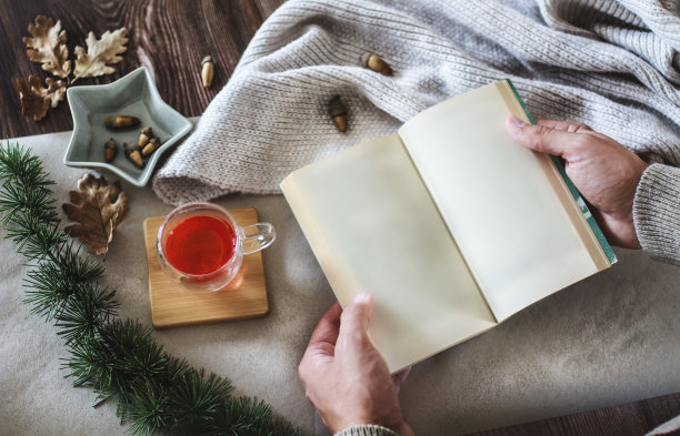 男人的手拿着空页的书，在家里冬天的田园诗，热茶和毯子图片下载