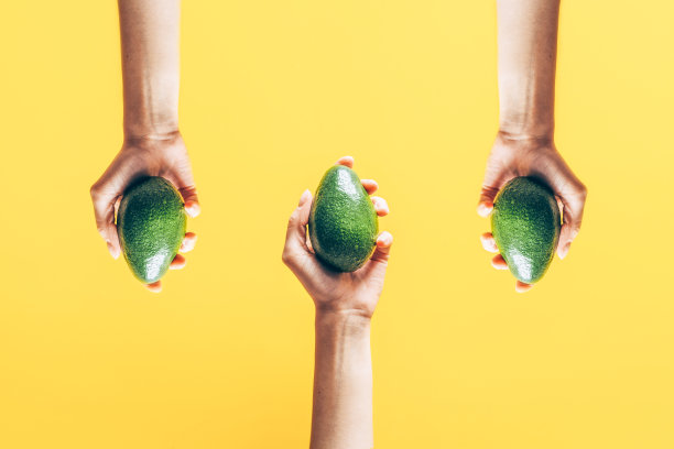 俯视图的妇女手拿牛油果在黄色背景。图片下载