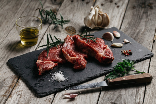 特写镜头生牛肉片在杂乱的餐桌上与迷迭香和大蒜图片下载