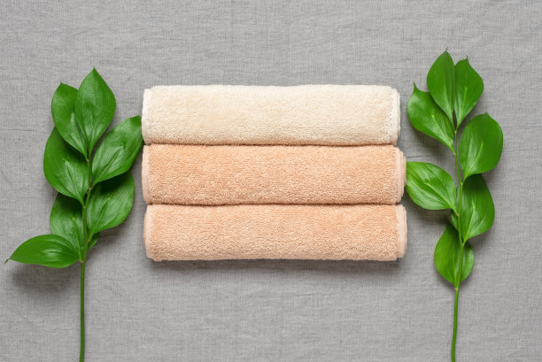 米色毛巾布卷和绿色的红果叶在灰色的亚麻纺织背景。俯视图，平铺。图片下载