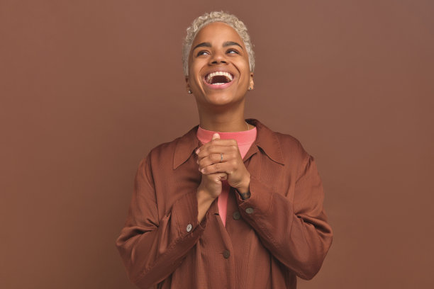 年轻的笑着的非裔美国妇女握紧手掌在胸前抬起下巴图片下载