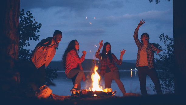 快乐的多民族朋友在周末的森林旅行中围着火跳舞。年轻人在玩乐，火焰在移动。图片下载