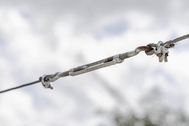 米色墙壁背景下的金属电缆拉紧建筑结构的松紧扣。用于拉紧电缆和其他设备的建筑工具特写图片下载