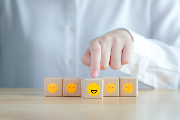 用手指着木块上不快乐的面孔中的快乐的面孔。积极思考、反馈、满意度、客户服务审查、精神健康评估、世界精神卫生日概念。图片下载