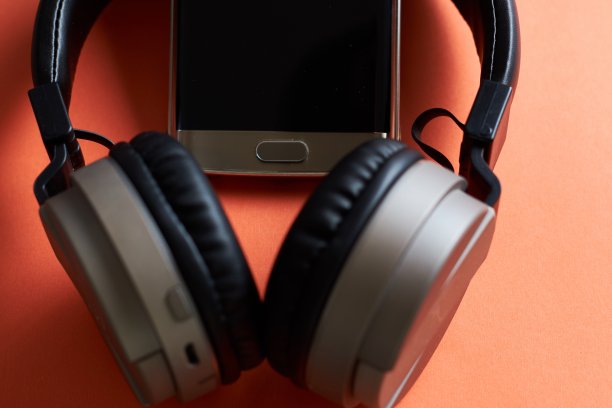 橙色表面上的无线耳机和手机特写镜头图片下载