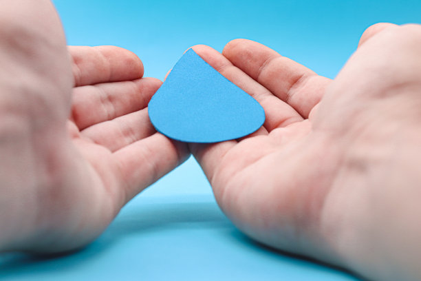 手拿着蓝色背景上的纸水滴。节约用水，抗旱，世界水日，洗手液卫生，家庭洗手，CSR，节约用水，清洁可再生能源滴图片下载