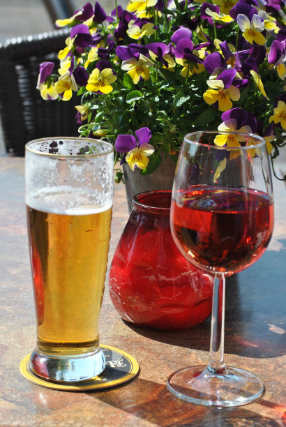 特写镜头的一杯葡萄酒和啤酒与花瓶中的花为背景图片下载