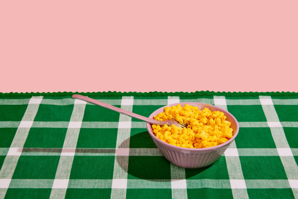 健康饮食。美食波普艺术摄影。一个大碗，装着甜玉米罐头，放在格子桌布上，粉色的背景隔开。食物的概念，创造力。图片下载