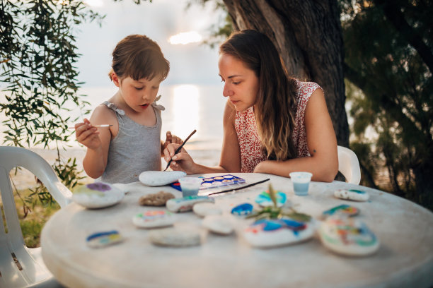 母女俩坐在海边，在岩石上画画，玩得很开心图片下载