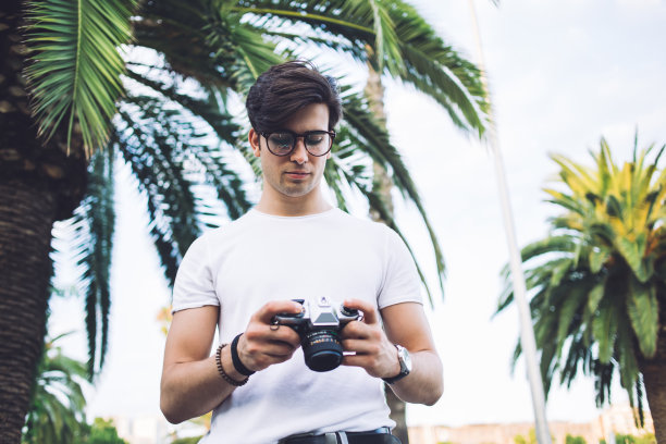 严肃的白人男子穿着时髦的服装在户外度过空闲时间在市中心拍摄业余照片，沉思的男性游客20岁带着相机检查照片探索地点和目的地图片下载