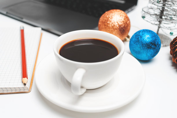 咖啡杯在白色的桌子与笔记本电脑和圣诞装饰，近距离观看图片下载