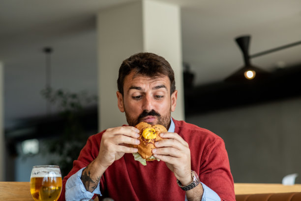 在一天的辛苦工作后，有魅力的商人吃着汉堡喝着啤酒图片下载