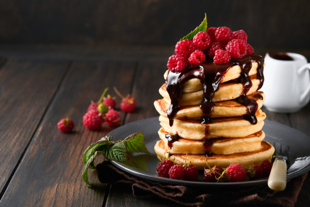 煎饼。薄煎饼与新鲜覆盆子巧克力釉或浇头在灰色的碗在旧木桌背景。自制的经典美式煎饼。页面为杂志概念。图片下载