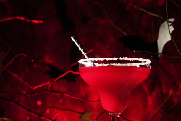 万圣节该死的鸡尾酒玛格丽塔。血红色的鸡尾酒玛格丽塔和瓶子形成的头骨在可怕的红色深色背景。派对上的节日饮料，有糖果眼睛，蝙蝠，蜘蛛。亡灵节。图片下载