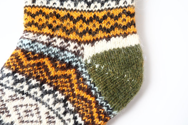 针织羊毛袜上图案装饰的碎片。冬天的动机。米色，棕色，白色，绿色，黑色手工编织线。针织鞋跟与手编缝。白色背景图片下载