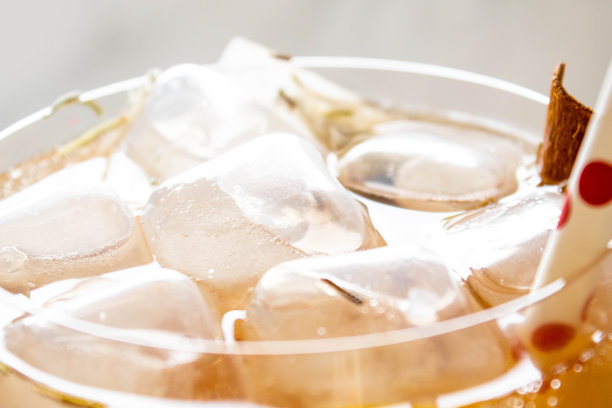 柠檬冰茶装在玻璃杯里，加冰块，白色纸吸管，大理石背景上有红球。提到保健、水果和植物的替代医学和茶点。图片下载
