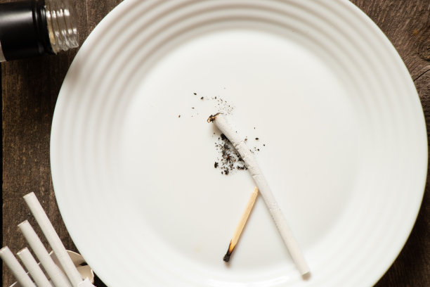 碎香烟放在盘子上，瓶子旁边的桌子上，吸烟和酗酒的坏习惯图片下载