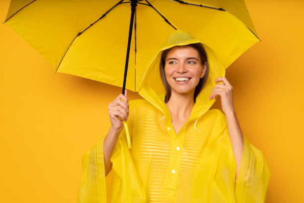 女人站在伞下穿着防水雨衣黄色背景图片下载
