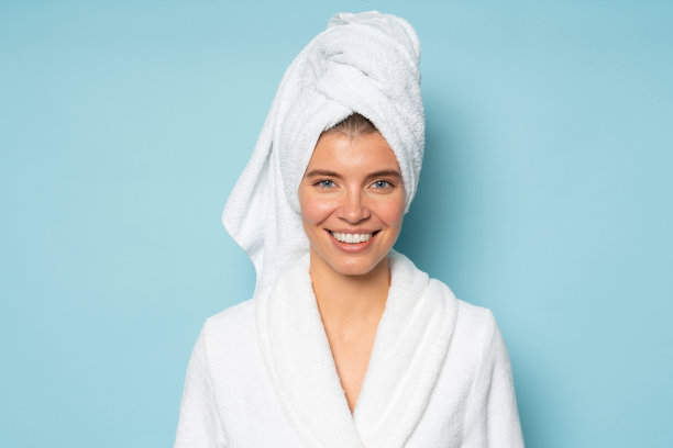 特写肖像的女人在蓝色背景与头部浴巾穿着浴袍图片下载
