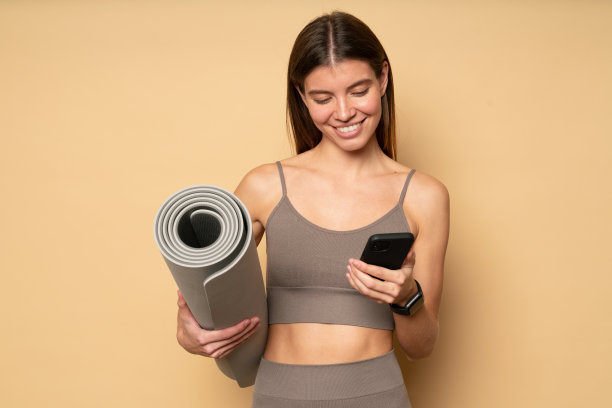 健身女子在训练结束后，手拿手机和卷垫与男友在网上聊天图片下载