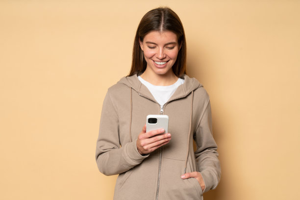 女子健身教练浏览手机应用程序在棕色背景与手在口袋的运动卫衣图片下载