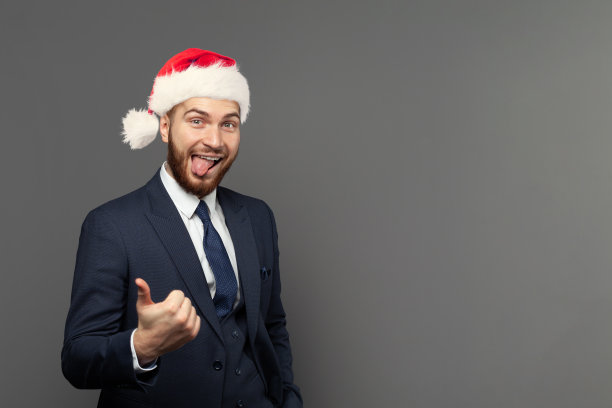 画像的快乐快乐的商人在圣诞帽举行大拇指在灰色的墙壁背景图片下载