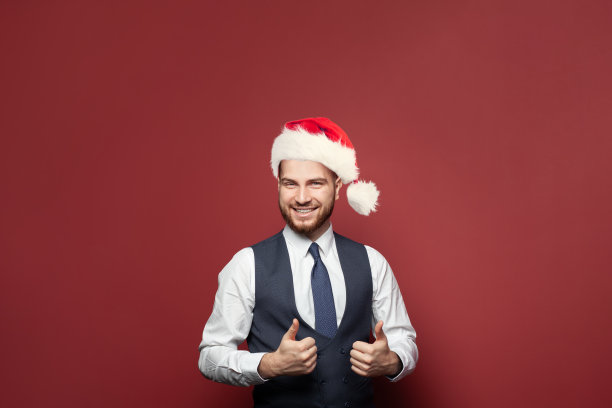 快乐乐观的商人在圣诞帽微笑和展示拇指对红色的工作室墙横幅背景图片下载