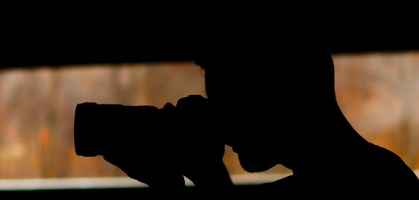 一个拿着相机的男人在栅栏前拍照的侧影图片下载