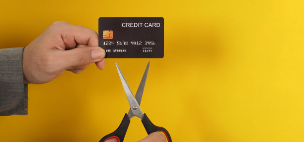 手握黑色信用卡和黄色背景的剪刀。男人穿着一套灰色的西装图片下载