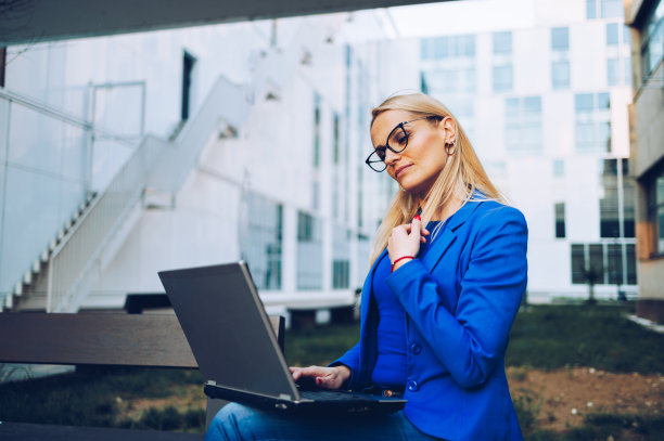 现代女商人一边在公司大楼前工作，一边用笔记本电脑进行视频通话图片下载