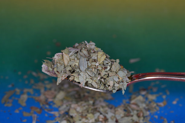 在灯光和彩色模糊的背景下，汤匙上的干塞纳茶叶的特写图片下载