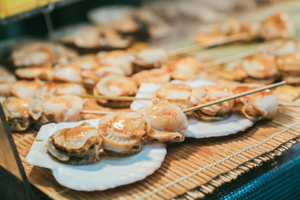 在日本大阪的黑门市场，美味的扇贝肉棒和酱汁放在贝壳和竹桌垫上图片下载
