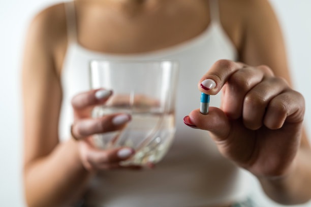 裁剪的照片，一个美丽的年轻女孩，一只手拿减肥药，另一只手拿玻璃杯。图片下载