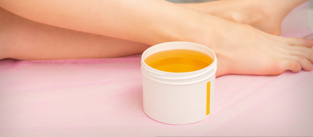 在水疗中心脱毛前，女子用白色的蜜蜡罐抹腿。图片下载