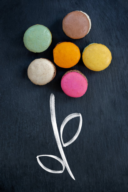 黑色石板背景上花朵形状的法式马卡龙，创意美食装饰概念图片下载