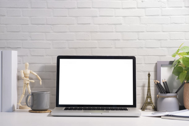 前视图笔记本电脑，咖啡杯，笔记本和室内植物在白色的桌子上。空白屏幕为您的广告文字。图片下载