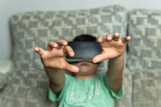 一个黑头发的男孩带着他的虚拟现实眼镜，把他的手放在前面试图触摸生成的3D空间。图片下载