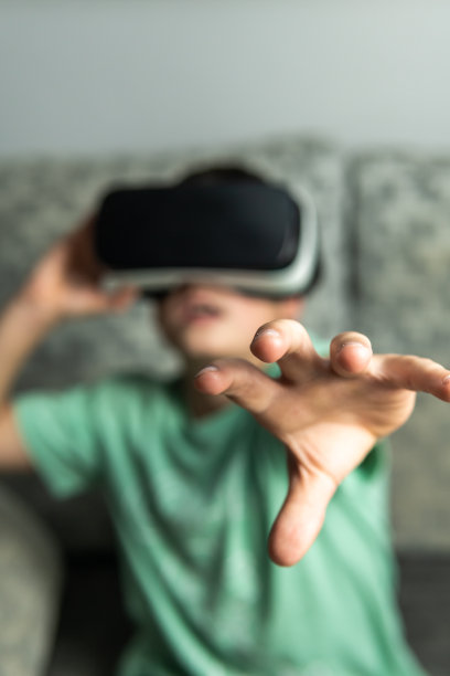 正面垂直拍摄的一个黑头发男孩拿着他的虚拟现实眼镜，把一只手放在前面触摸生成的3D空间。图片下载