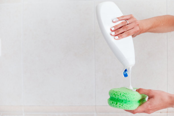 女人的手把一瓶沐浴露压在柔软的绿色泡芙或海绵上洗澡。, copyspace图片下载