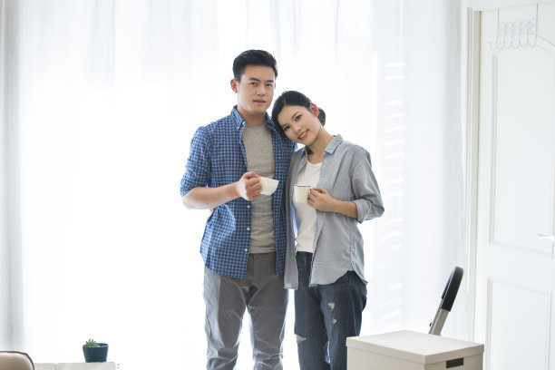 年轻夫妇刚搬进新家装饰的房间，依偎在一起喝咖啡，享受片刻的宁静——库存照片图片下载